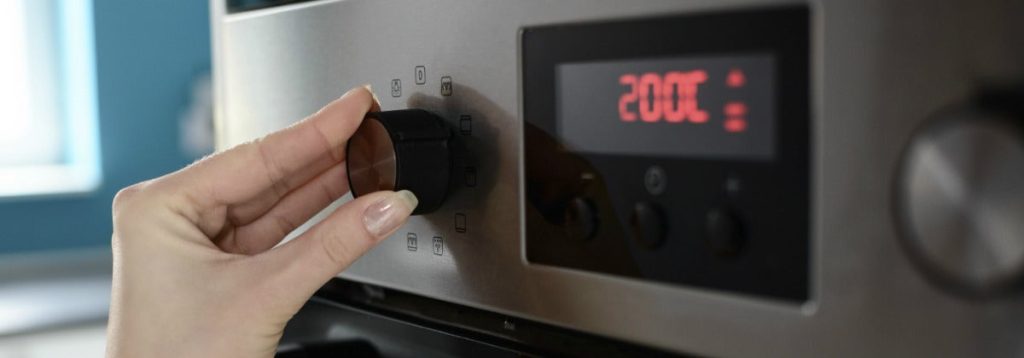 A hand adjusting a dial on a stainless steel oven, with the digital display showing a temperature of 200 degrees Celsius, preparing the perfect environment to roast veggies glazed with sweet local honey. A hand adjusting a dial on a stainless steel oven, with the digital display showing a temperature of 200 degrees Celsius, preparing the perfect environment to roast veggies glazed with sweet local honey.