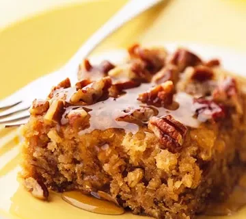 A slice of moist cake topped with pecans and drizzled with sweet local honey sits on a yellow plate with a fork beside it.