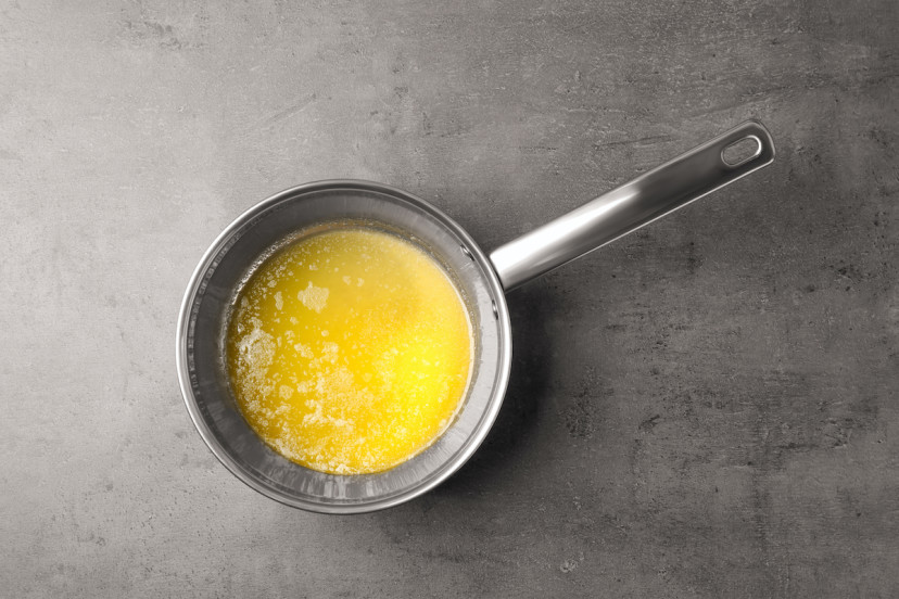 A saucepan containing melted butter and sweet local honey is placed on a gray, textured surface. A saucepan containing melted butter and sweet local honey is placed on a gray, textured surface.